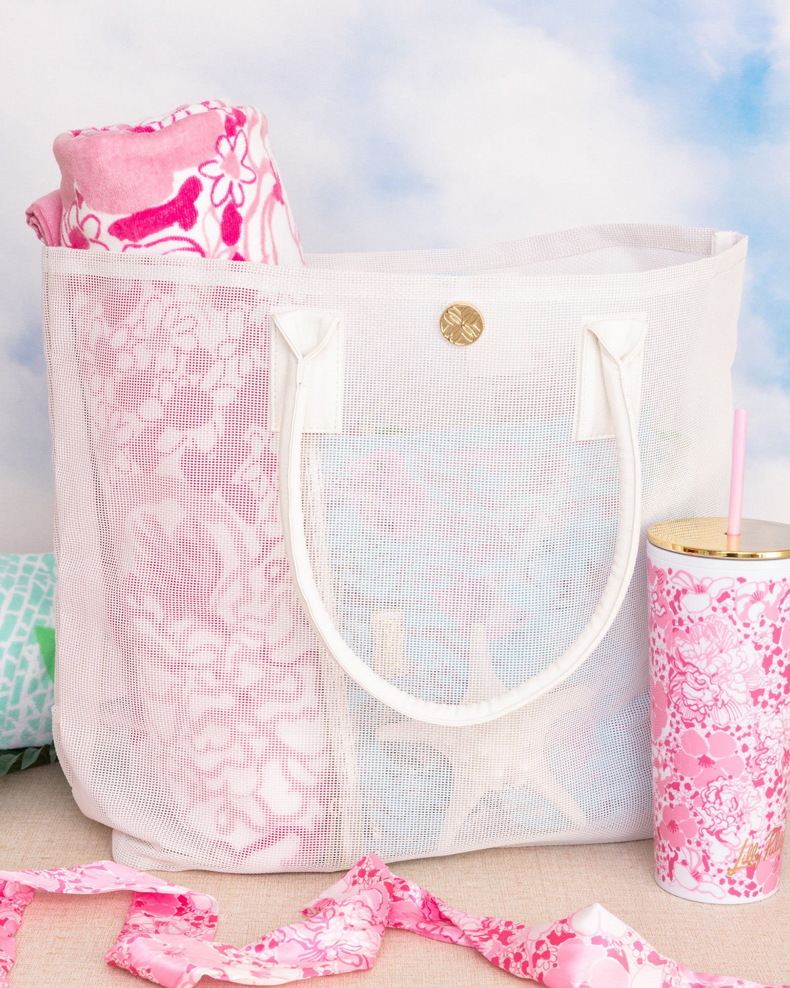 white mesh beach bag with a pink floral towel and matching tumbler