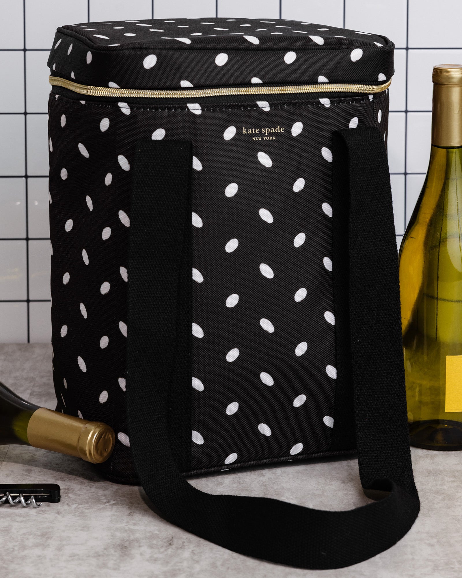 Black polka dot wine cooler bag with bottles and a corkscrew on a tiled wall background