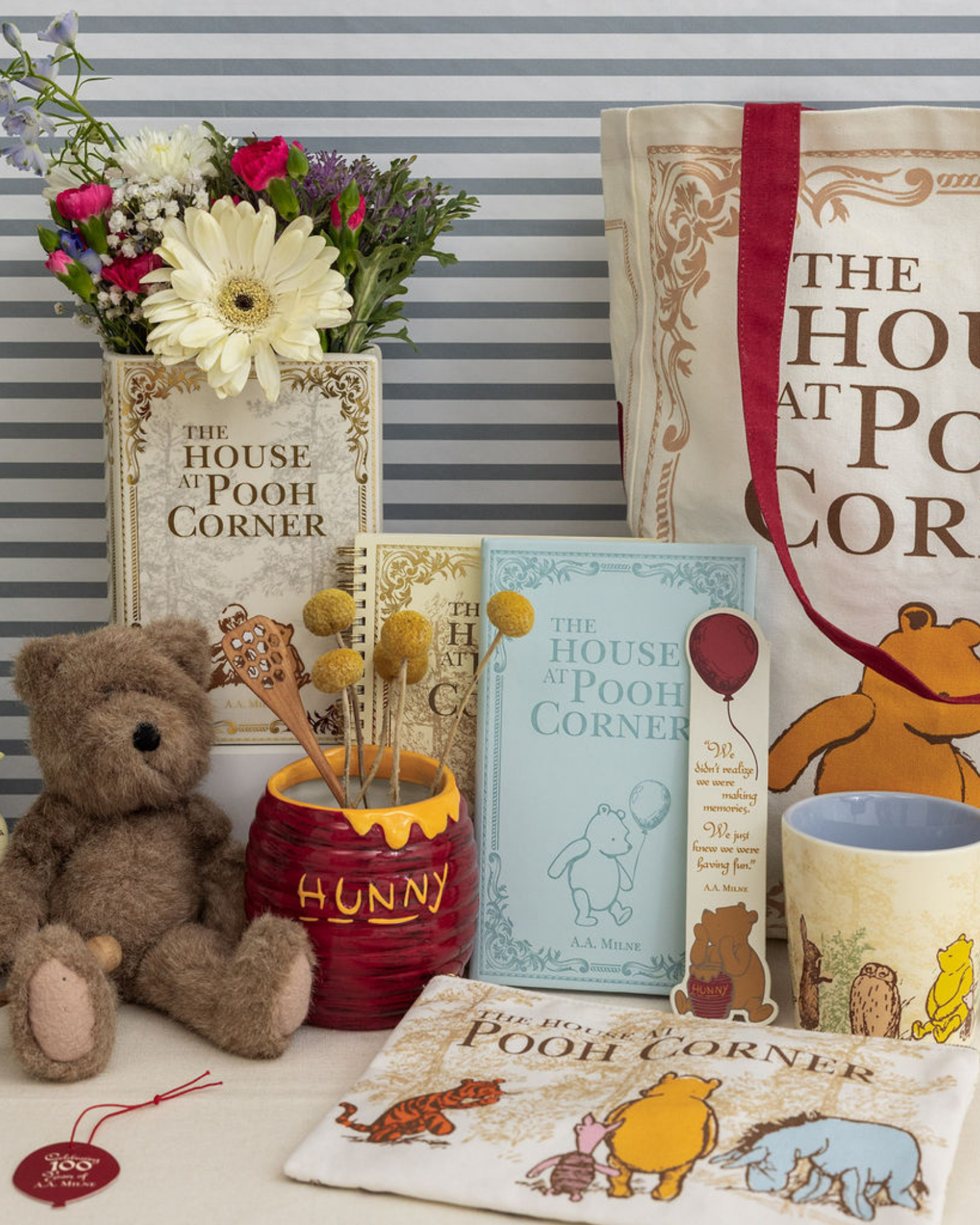 Collection of Winnie the Pooh-themed items including a teddy bear, mug, and books on a striped background.