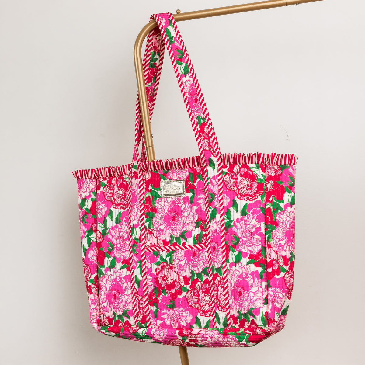 A bright pink tote bag with a floral print, featuring pink and white chevron-patterned handles and a small brand patch on the front.