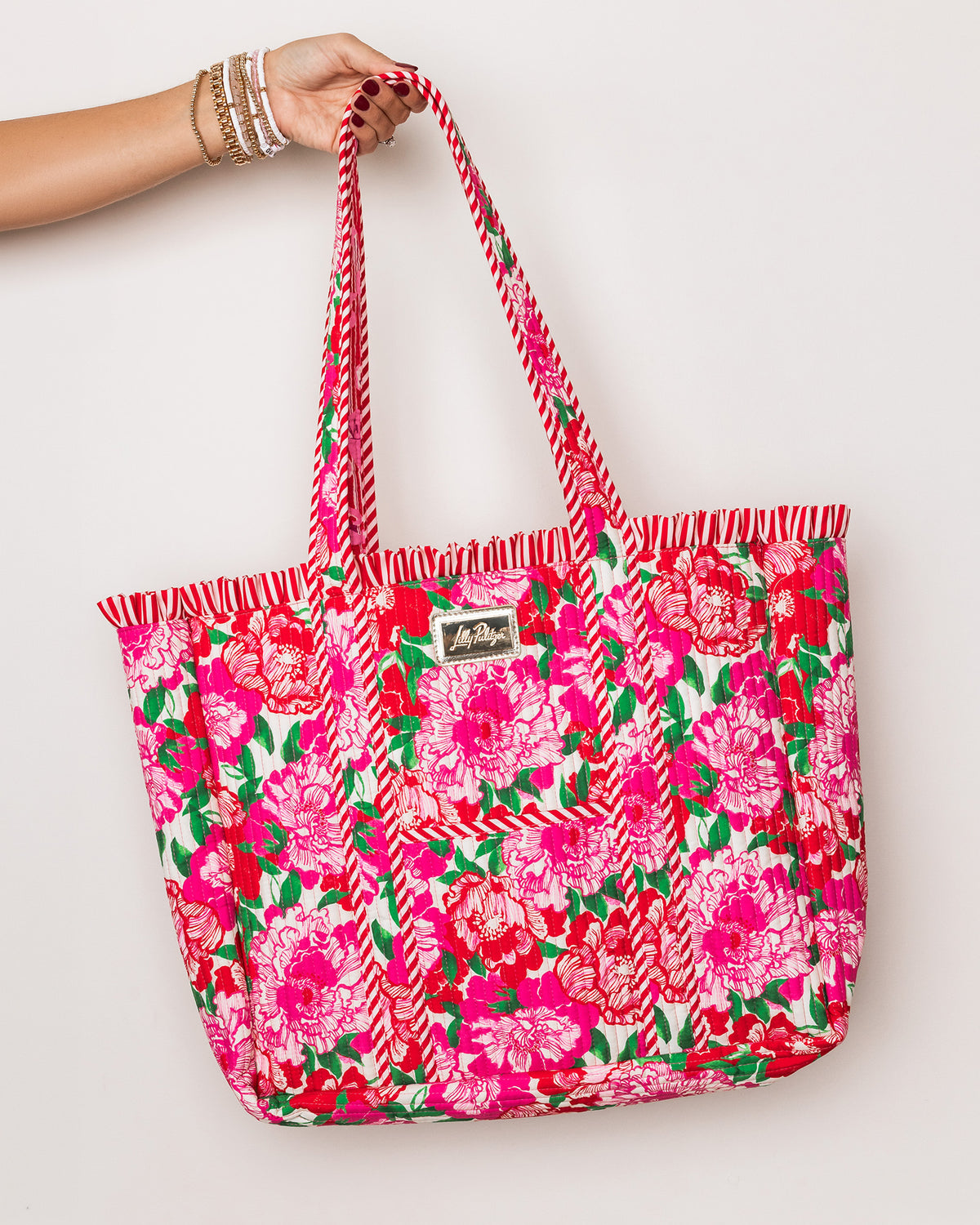 model holding bright pink tote bag with a floral print, featuring pink and white chevron-patterned handles and a small brand patch on the front.