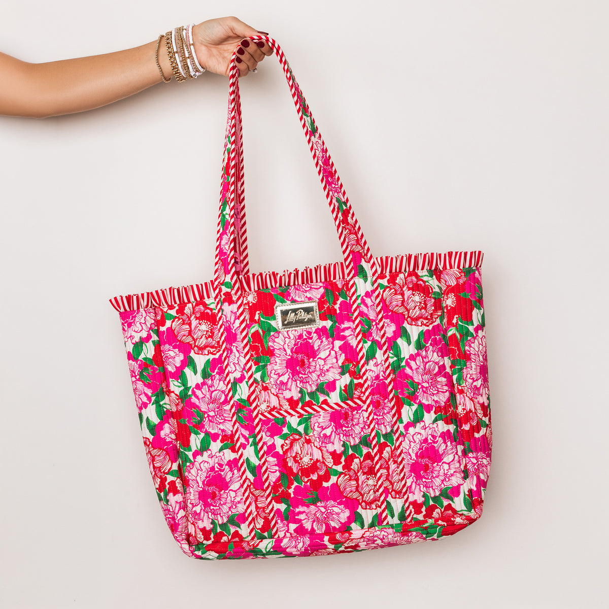model holding bright pink tote bag with a floral print, featuring pink and white chevron-patterned handles and a small brand patch on the front.