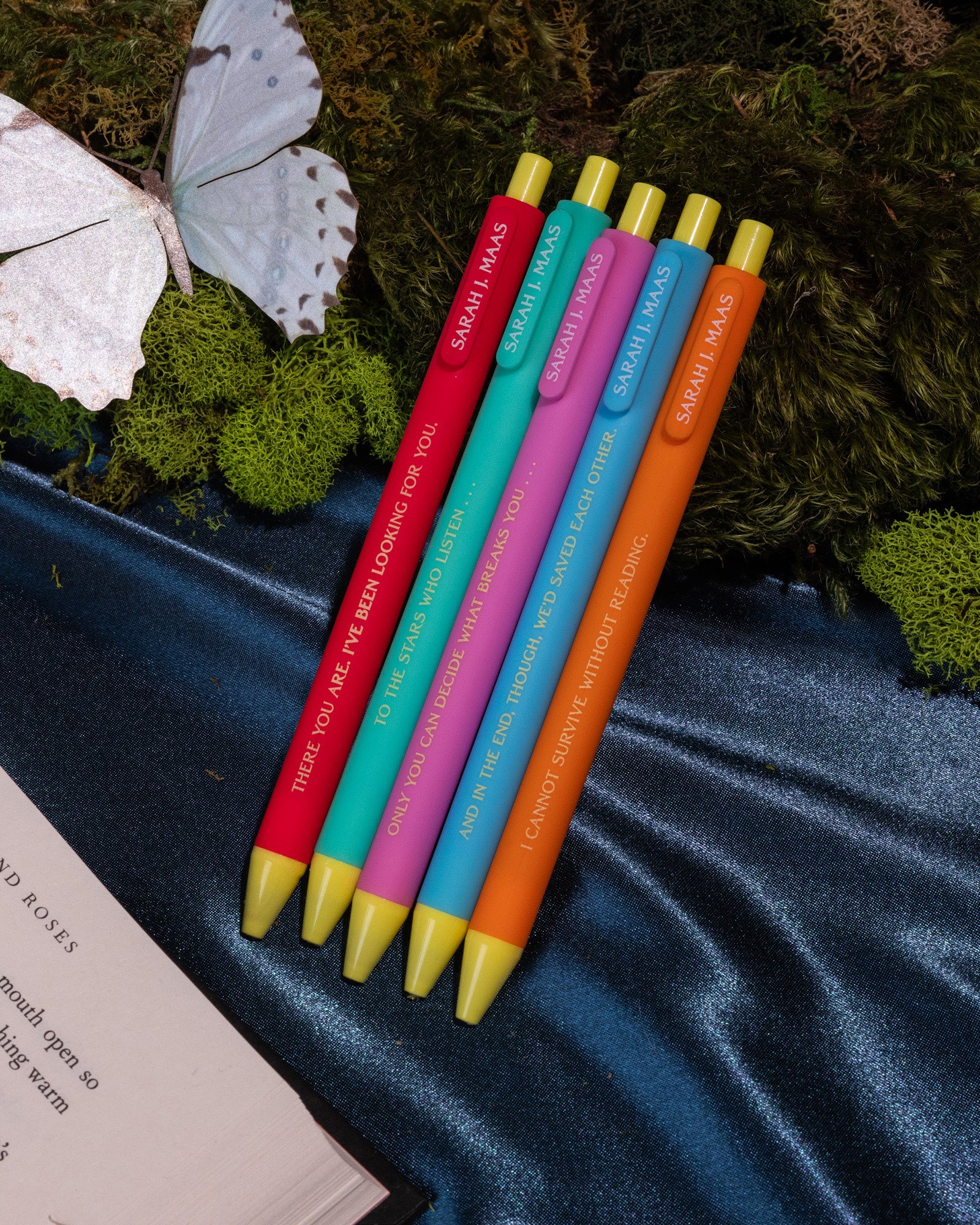 Five colorful pens with yellow tips on moss and a silky navy backdrop