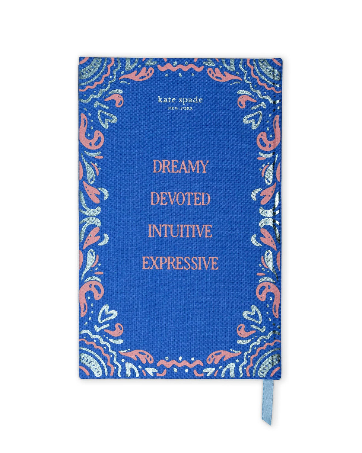 A blue hardcover journal by Kate Spade New York with a decorative paisley border in coral pink, light blue, and white, featuring the words 'DREAMY DEVOTED INTUITIVE EXPRESSIVE' in coral text. A light blue ribbon bookmark is visible on the right side, set against a plain white background.