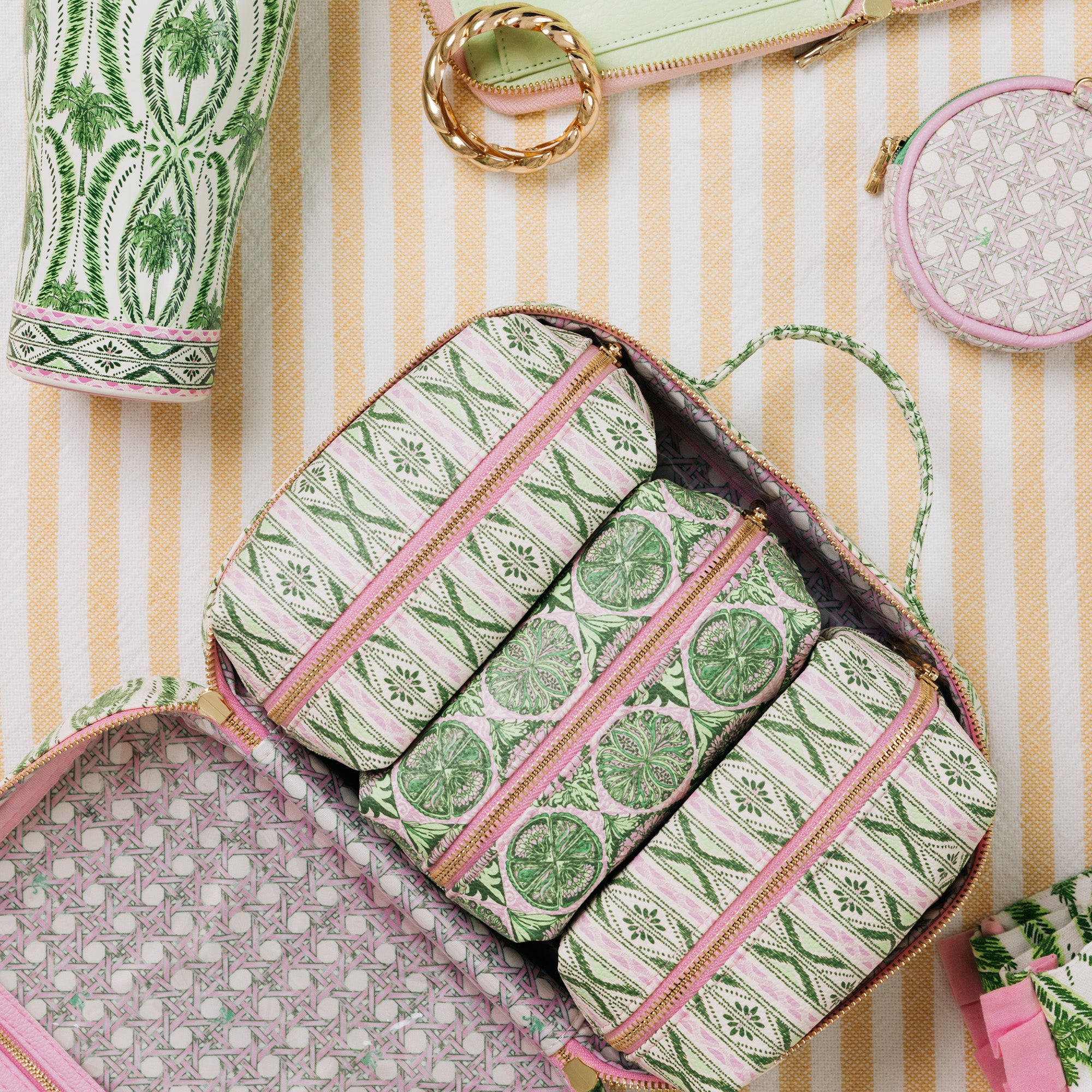 An open zippered cosmetic organizer bag filled with matching cylindrical pouches, shown in a styled flat-lay with other patterned accessories on a cream and tan striped surface.