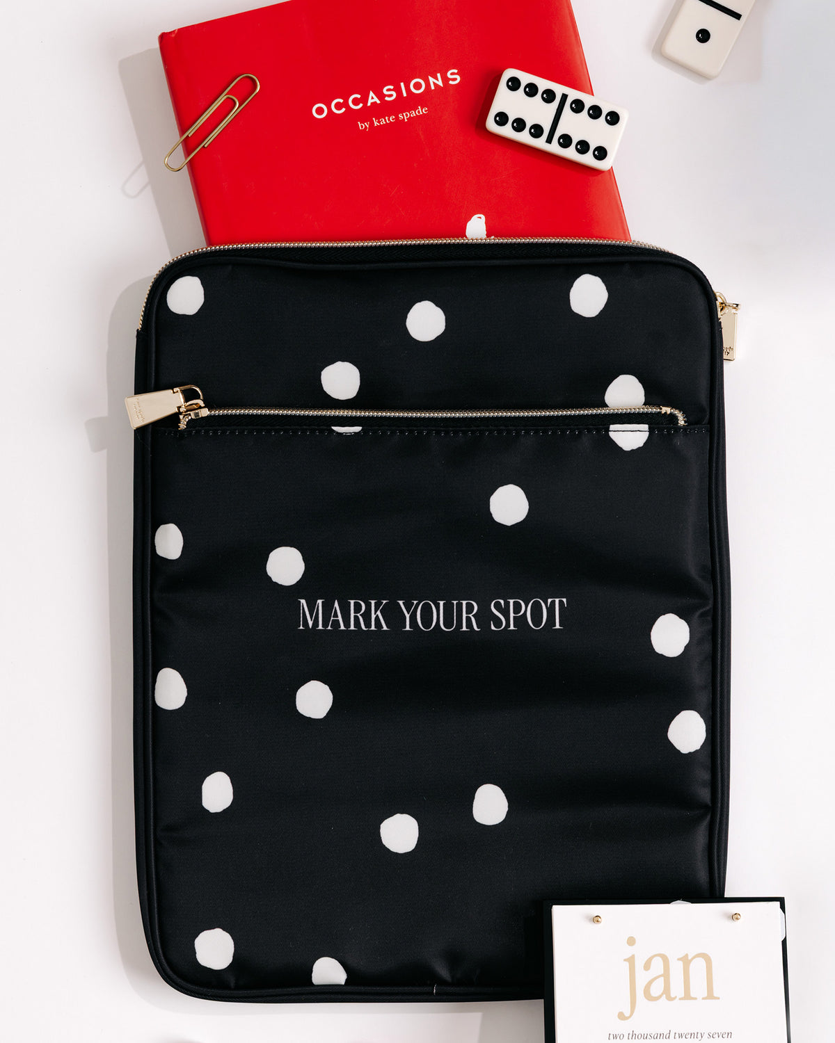 A black nylon tablet sleeve with white polka dots and the words 'MARK YOUR SPOT' printed in white, styled on a white background with a red notebook, paperclip, dice, and a hangtag.