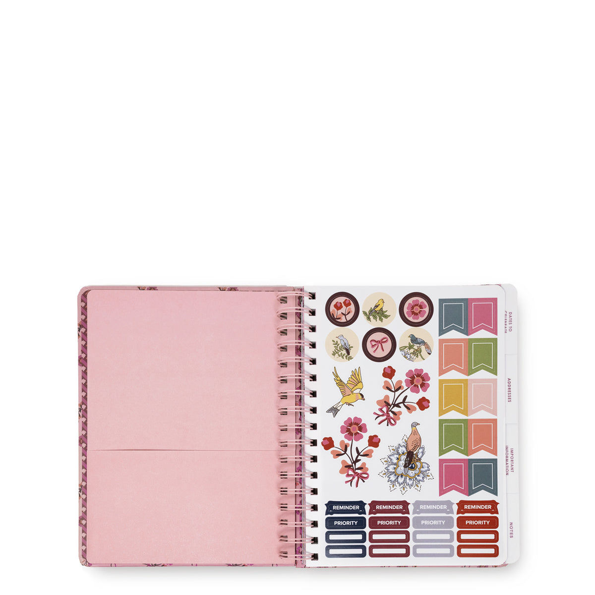 An open spiral-bound planner with a light pink cover on the left and a sticker sheet on the right, featuring colorful decorative stickers, birds, flowers, and label tabs against a white background.