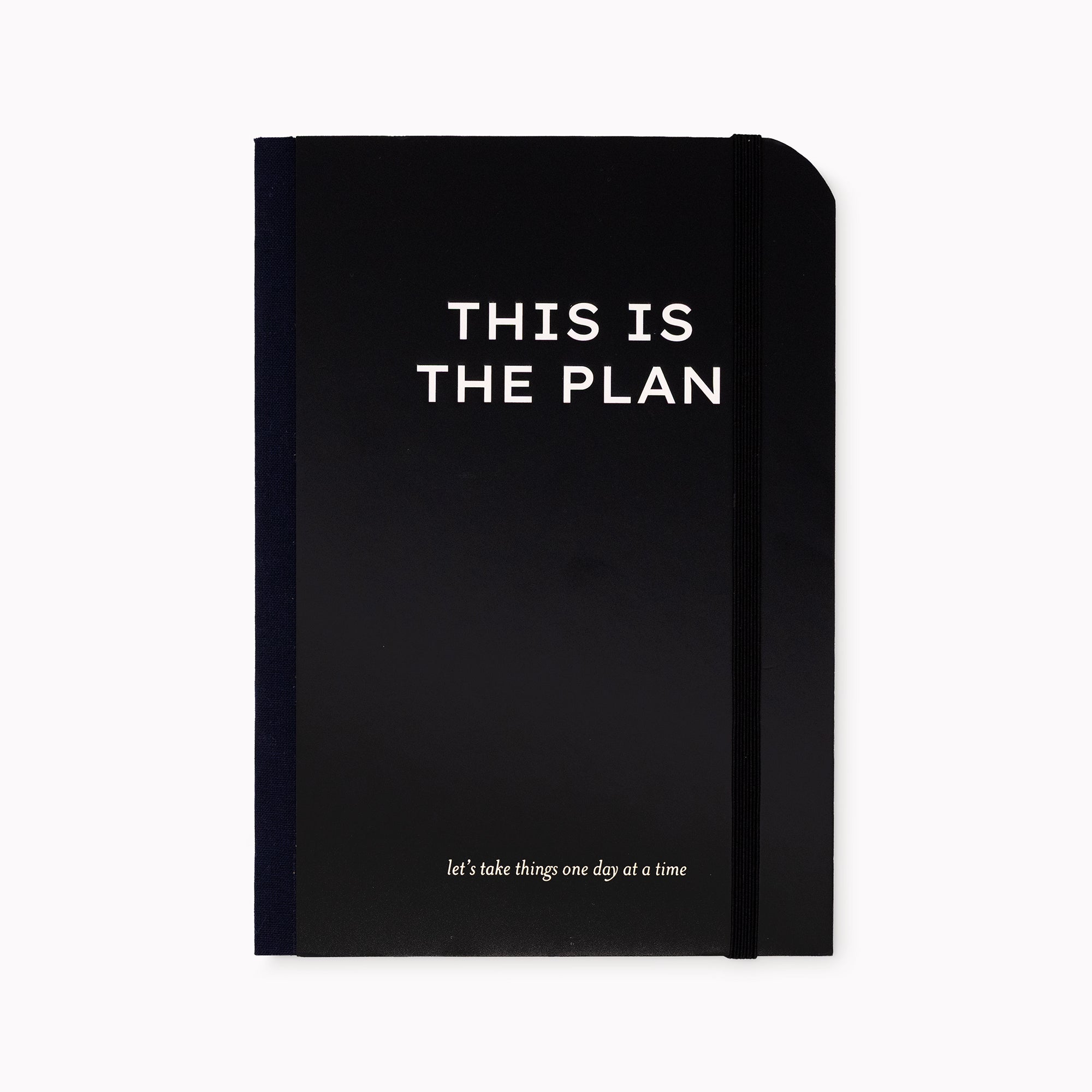 A black hardcover planner with white text reading 'THIS IS THE PLAN' and a smaller phrase near the bottom, shown on a plain light background.