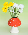 Red mushroom vase with yellow and white flowers on a green background