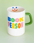White mug with colorful 'BOOK PERSON' text and a green handle on a light green background