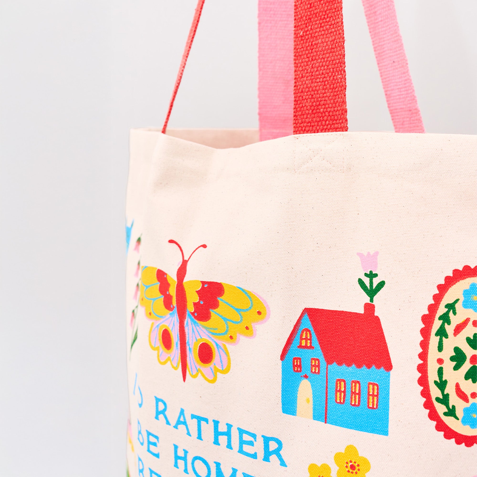 up close of cream tote bag with colorful icon graphic that says 'i'd rather be home reading'