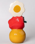 Colorful ceramic vase with a red apple, yellow smiley, and daisy on top against a light gray background