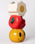 Colorful ceramic vase with stacked white daisy, apple, and yellow smiley on a white background.