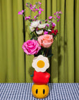 Colorful flower arrangement in a unique vase with a checkered tablecloth and green curtain background