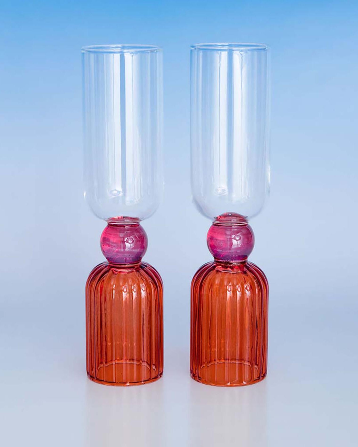 Two glass goblets with red bases and pink beads on a light blue background