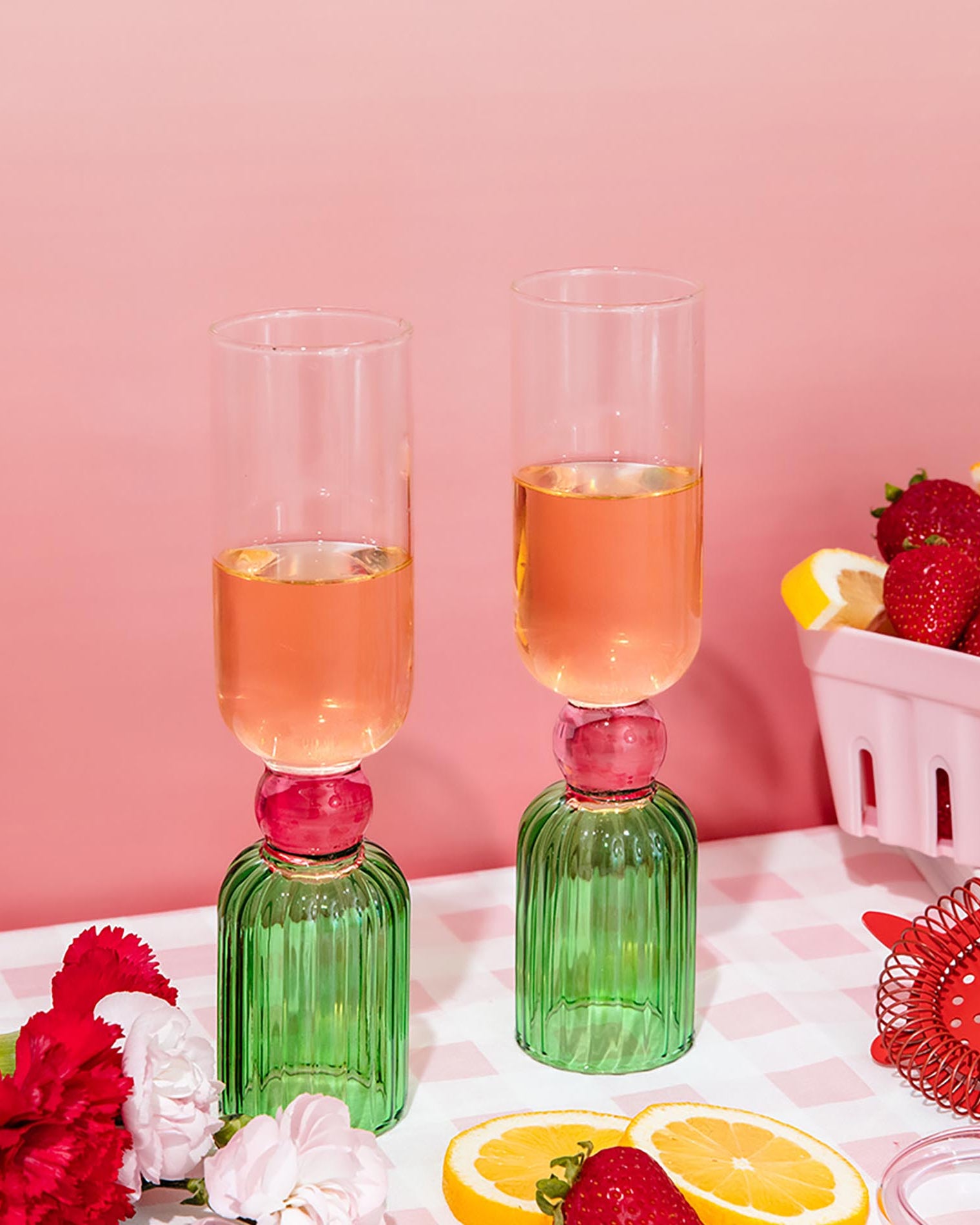 Two green glasses with pink liquid on a checkered tablecloth with strawberries and lemons.