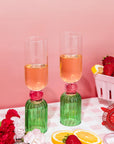 Two green glasses with pink liquid on a checkered tablecloth with strawberries and lemons.