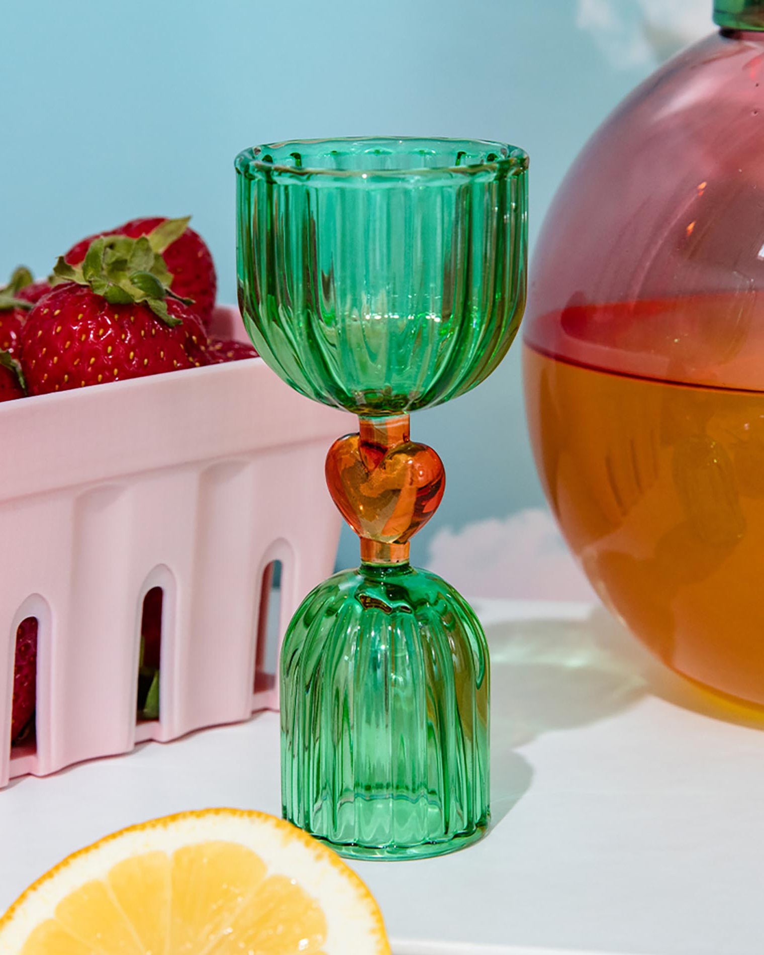 Green glass shot glass with yellow heart center on a white surface.