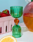 Green glass shot glass with yellow heart center on a white surface.