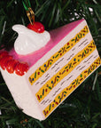 Decorative cake slice ornament with cherry on top hanging on a Christmas tree.