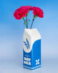 Oat milk carton vase with pink flowers against a blue gradient background