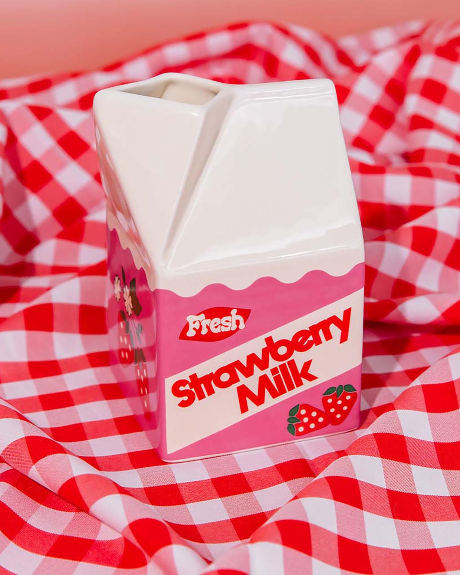Carton of strawberry milk vase on a red and white checkered tablecloth