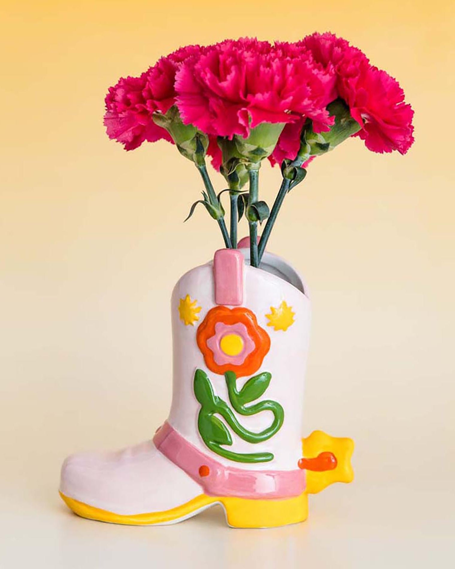 Decorative boot-shaped vase with pink flowers on a yellow background