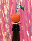 Cherry-shaped bottle stopper on a bottle with a colorful, blurred background