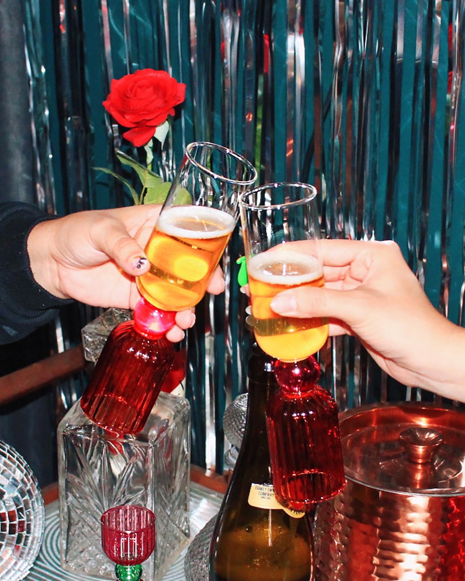 Two people clinking glasses with a decorative red rose in the background.