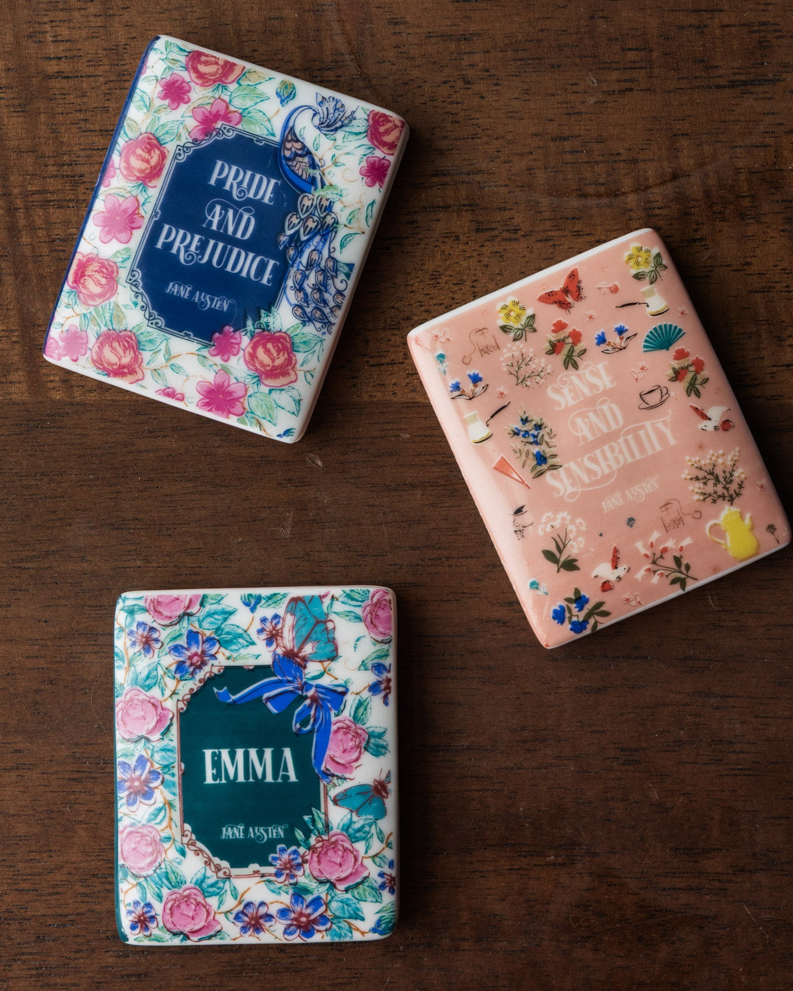Three book-themed magnets with floral designs and book titles on a white background