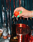 Hand using a cherry-themed bottle opener on a bottle with a festive background