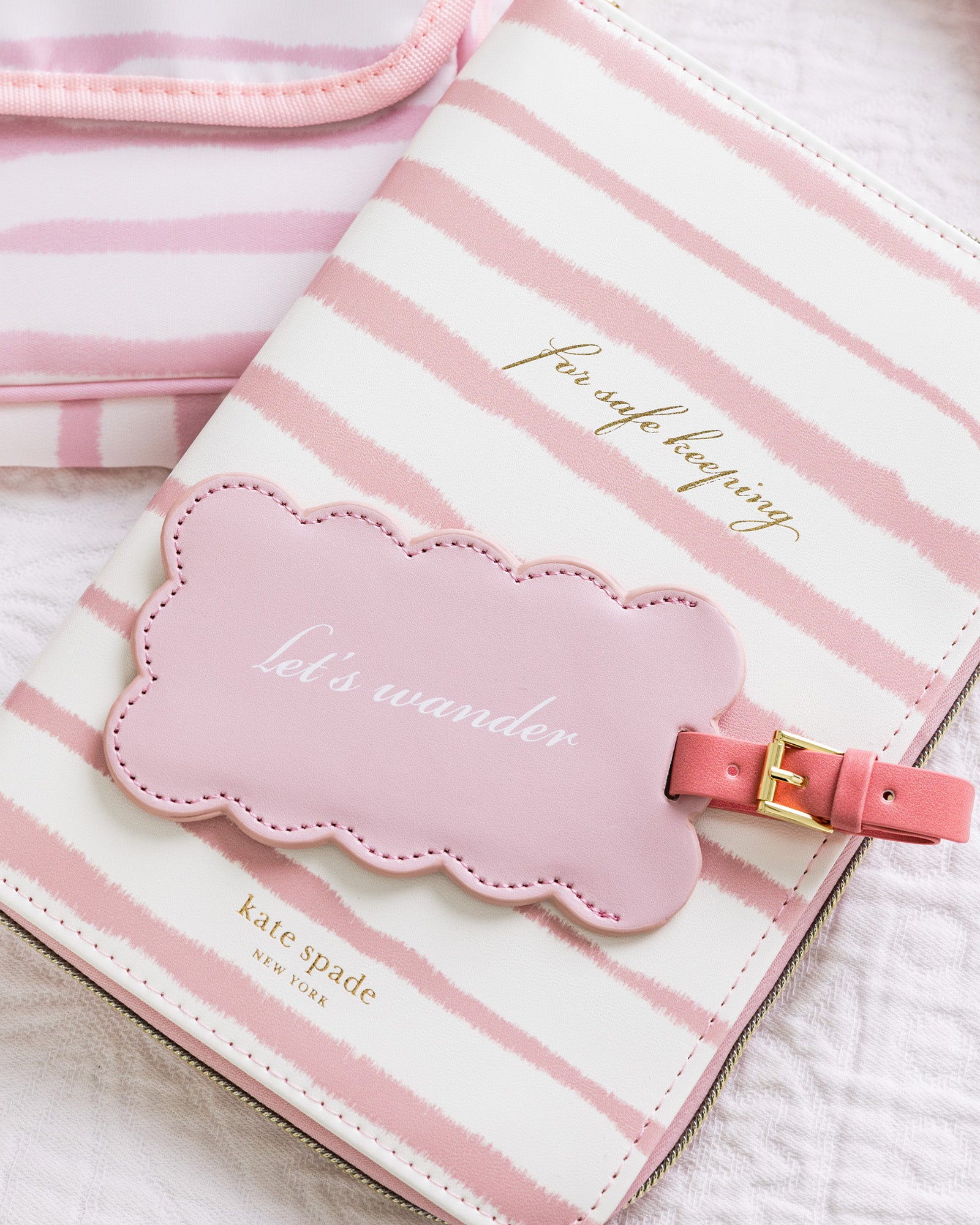 Pink and white striped travel pouch with a cloud-shaped tag on a light background