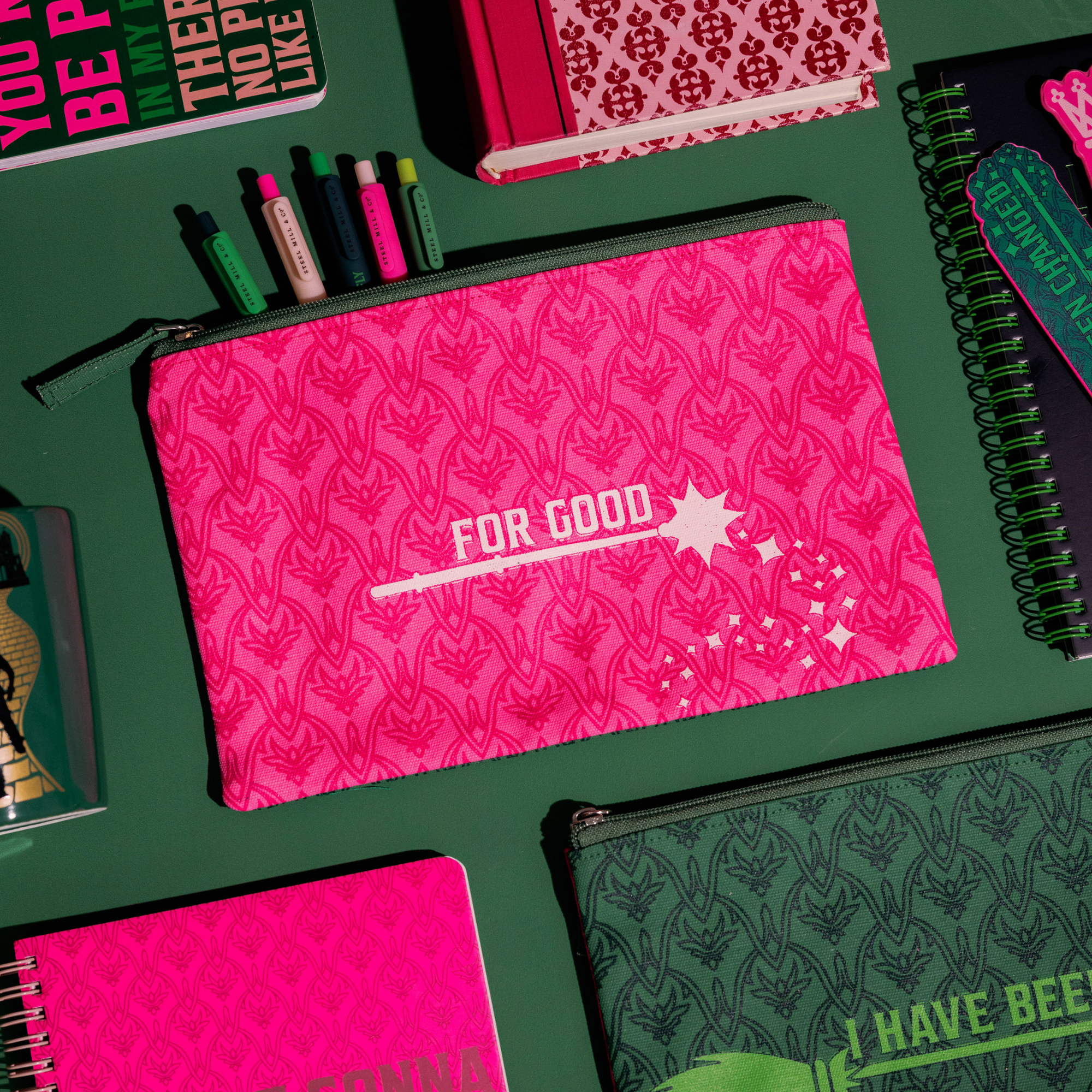 Pink pouch with 'FOR GOOD' text on a green background with stationery items.