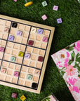 Sudoku board with colored numbers on grass, next to a floral notebook