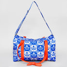 A blue and white patterned duffel bag with bright orange straps and a matching patterned shoulder strap, photographed against a light gray background.