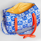 A blue and white patterned duffel bag with a bright yellow gingham interior and orange handles, shown on a light gray background.