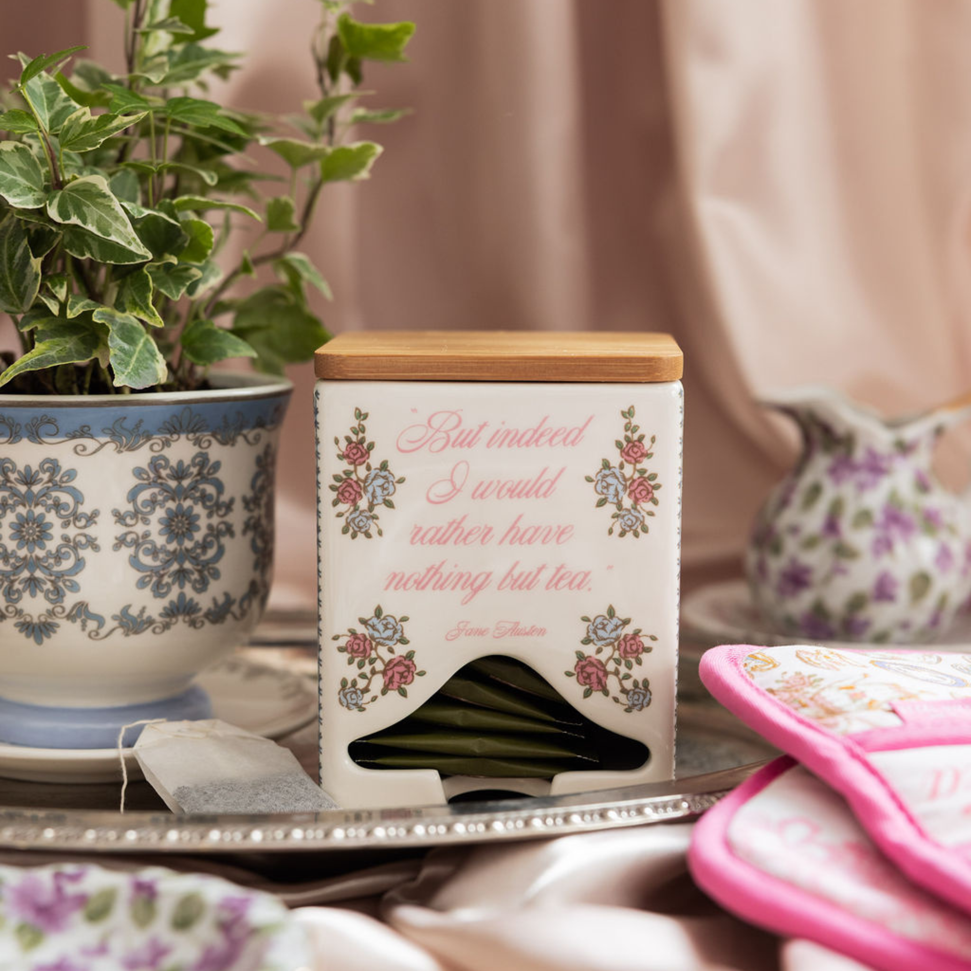 Tea bag container with floral design and text on a table with a plant and pink item in the background