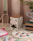Decorative items on a table including a candle, books, a plant, and a small table with floral design.