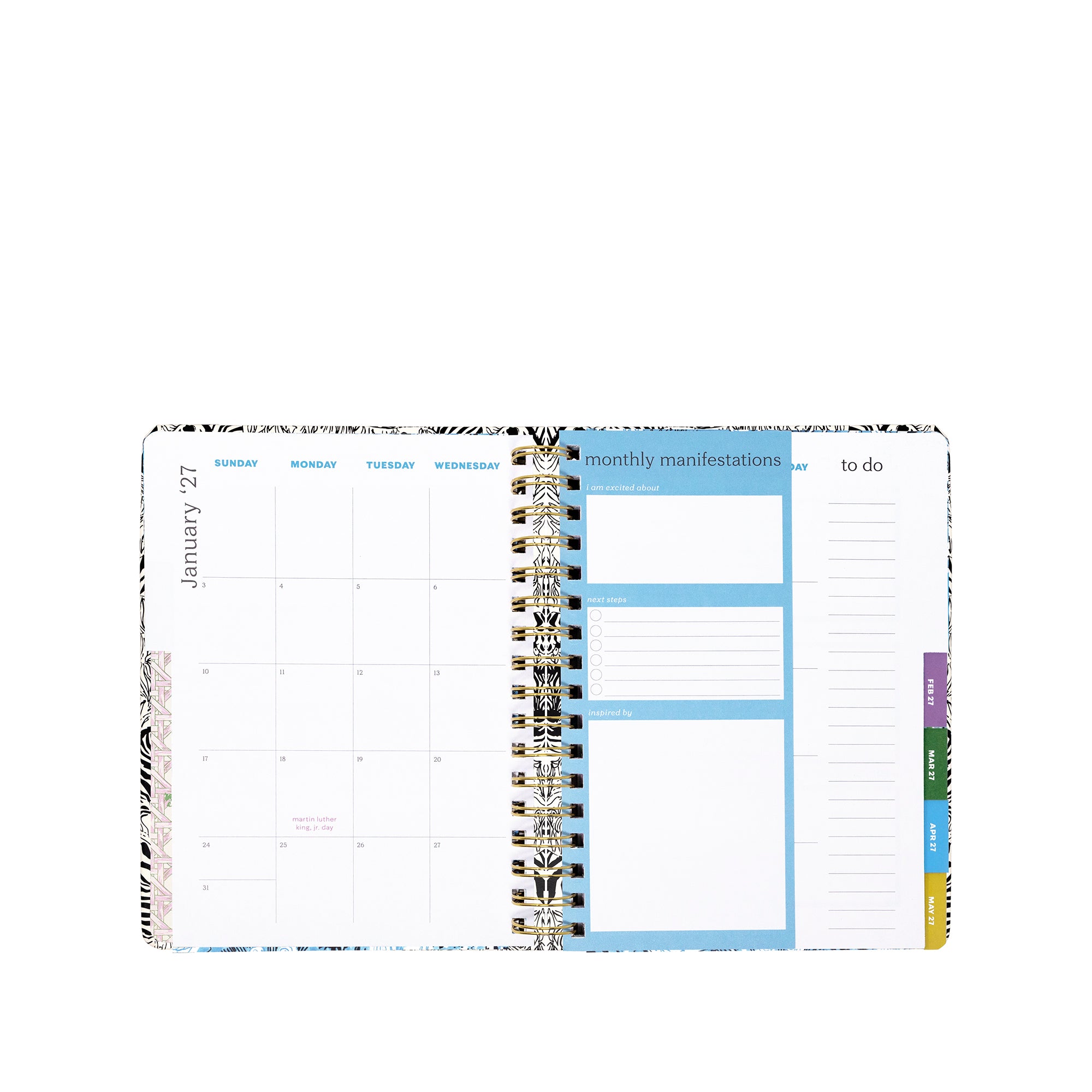 An open spiral-bound planner showing a monthly calendar page with blue highlighted sections, a monthly manifestations box, a to-do list, and colored tabs on the right.
