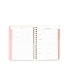 An open spiral-bound planner showing lined daily and weekly planning pages with pale pink accents on a white background.