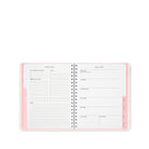 An open spiral-bound weekly planner page with pink and white pages, shown on a clean white background.