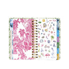 An open spiral-bound planner with a white cover featuring a pink tropical toile de Jouy pattern on the left page and small multicolored summer-themed illustrations on the right page. The pages are held together by gold-tone metal spirals, and colorful tabs are visible along the right edge.