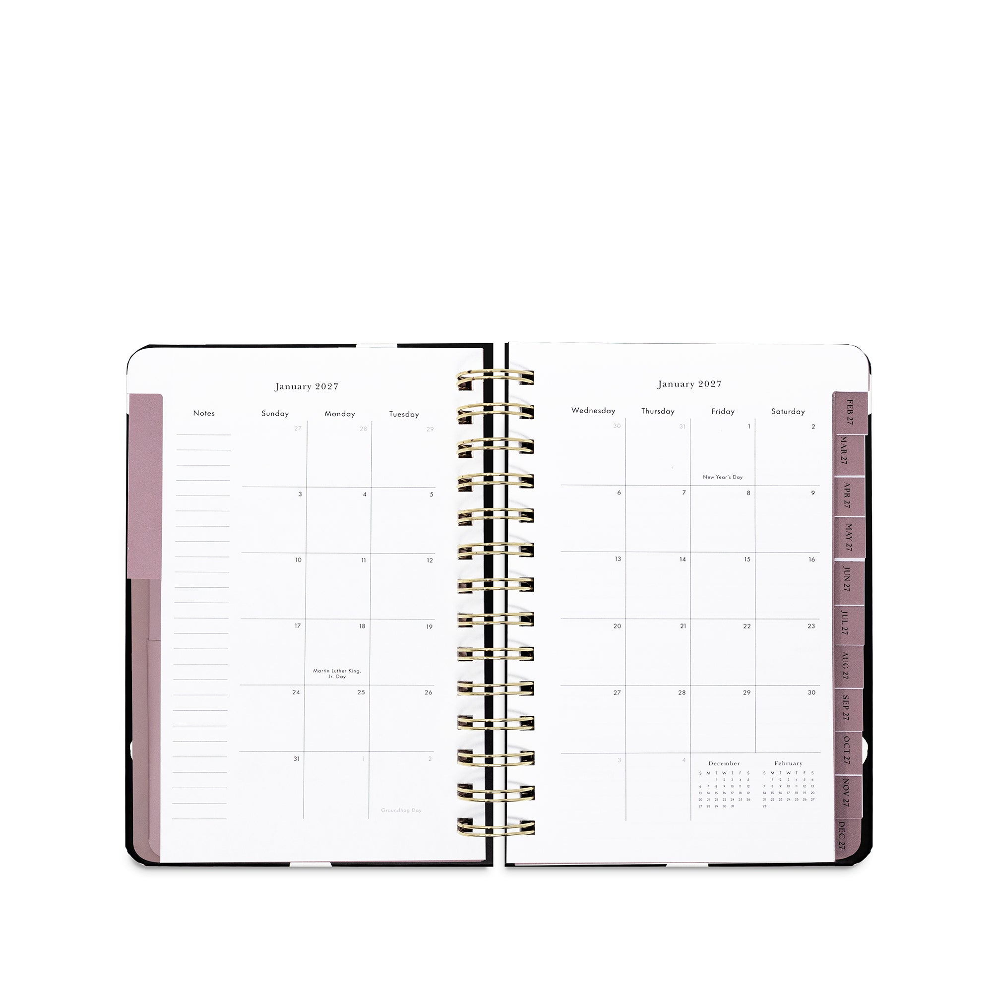 An open spiral-bound planner showing a monthly calendar layout in white pages with dusty pink sidebar accents and gold-toned wire binding, photographed on a clean white background.
