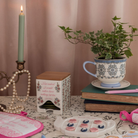 Decorative setting with a teacup, candle, books, and a plant on a table.
