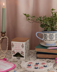 Decorative setting with a teacup, candle, books, and a plant on a table.