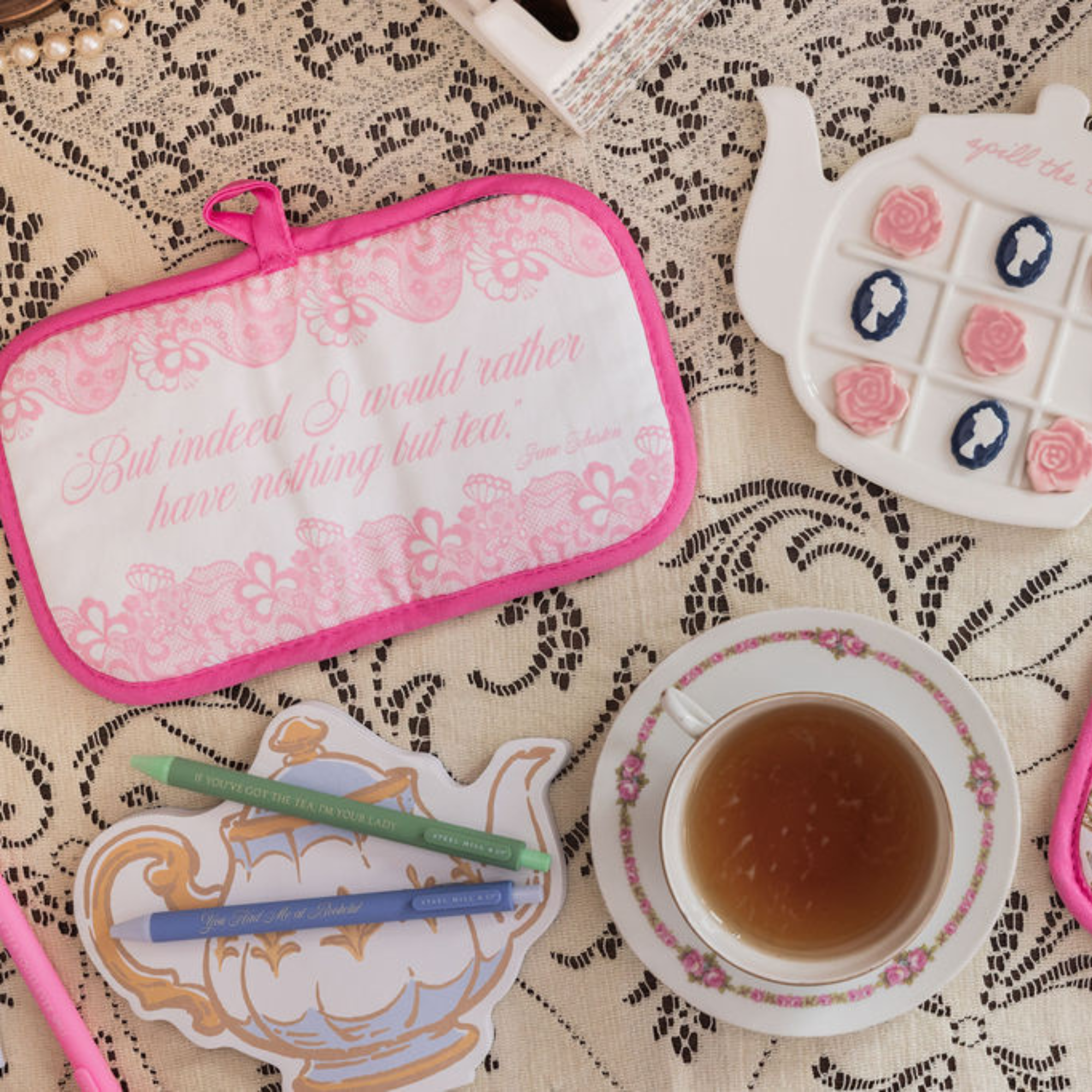 Tea-themed items including a pot holder, teacup, and teapot on a lace tablecloth.