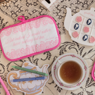 Tea-themed items including a pot holder, teacup, and teapot on a lace tablecloth.