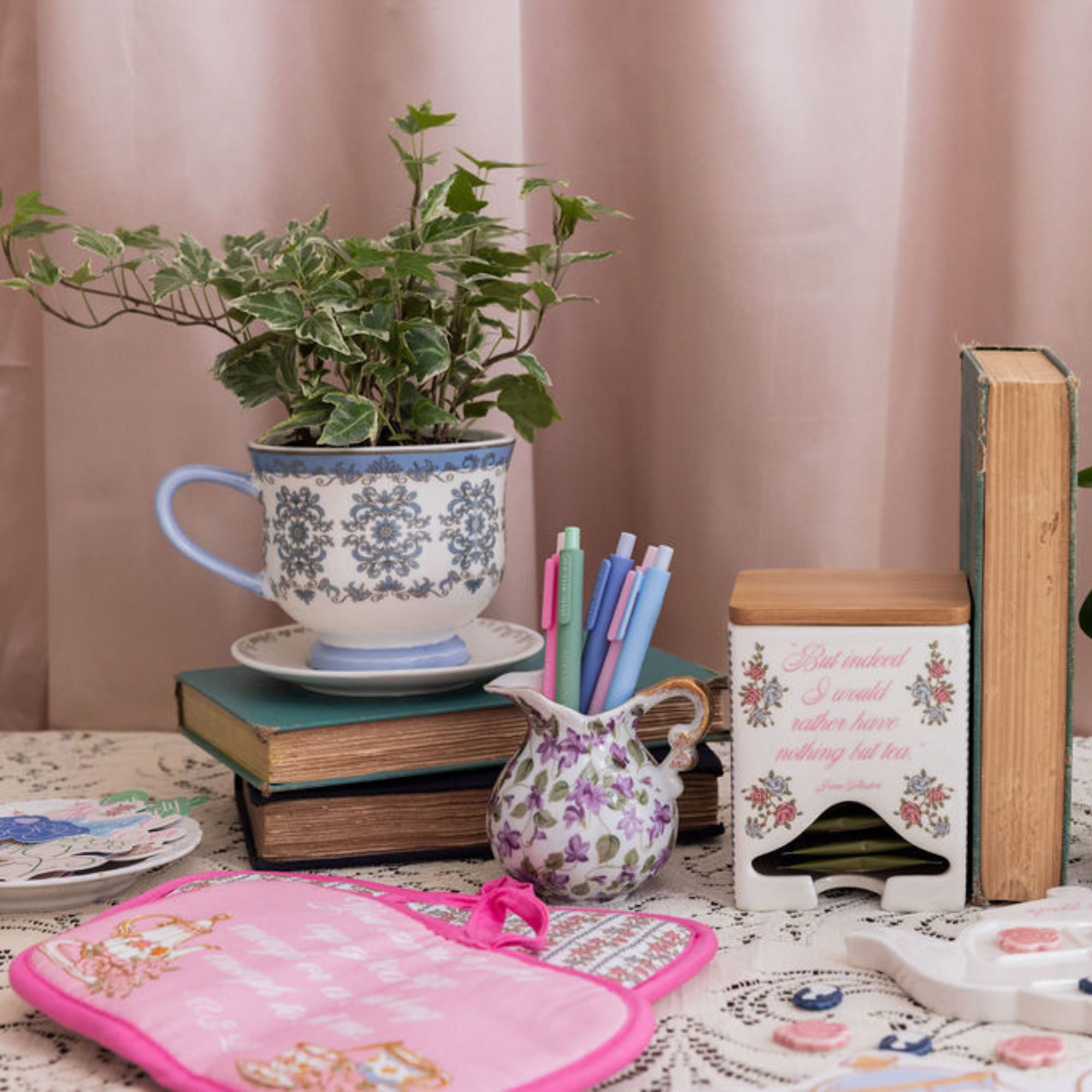 Decorative items including a teacup with plant, books, and a pink hot pad on a table.