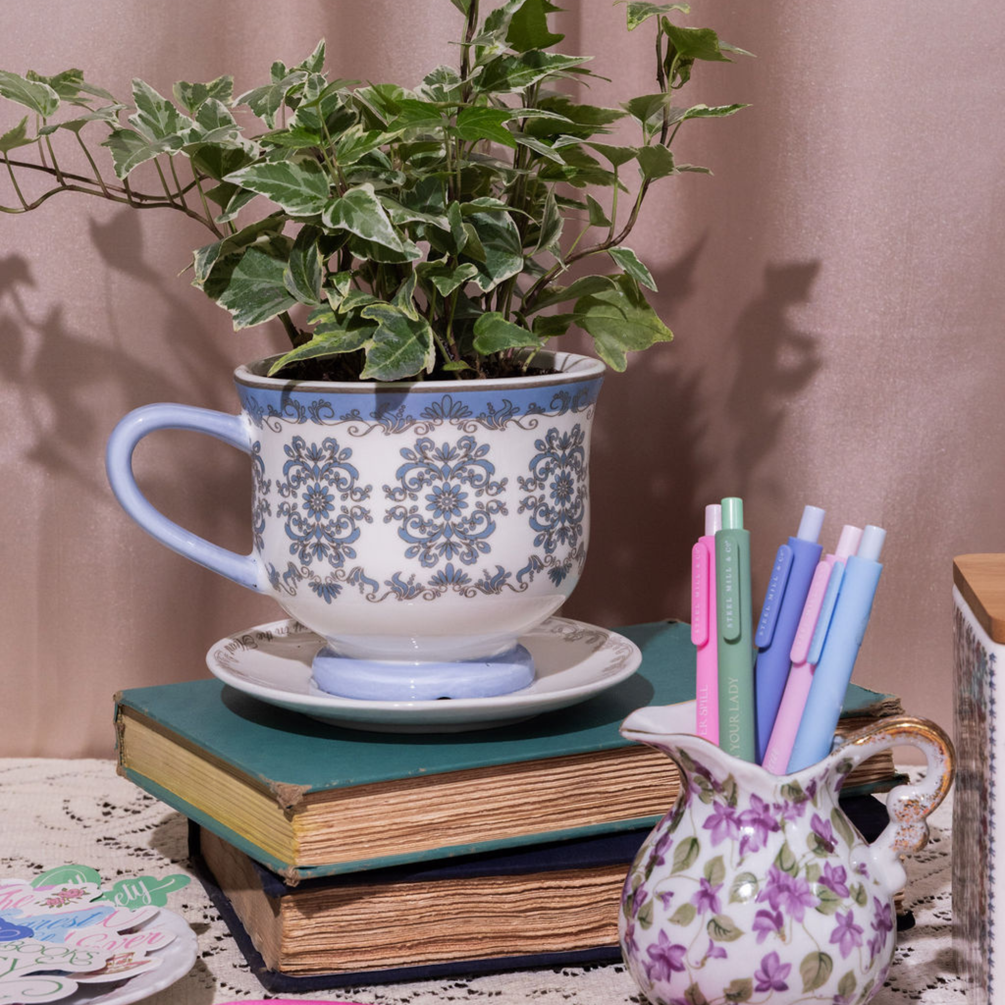 Decorative setup with a plant in a cup, books, and pens on a table.