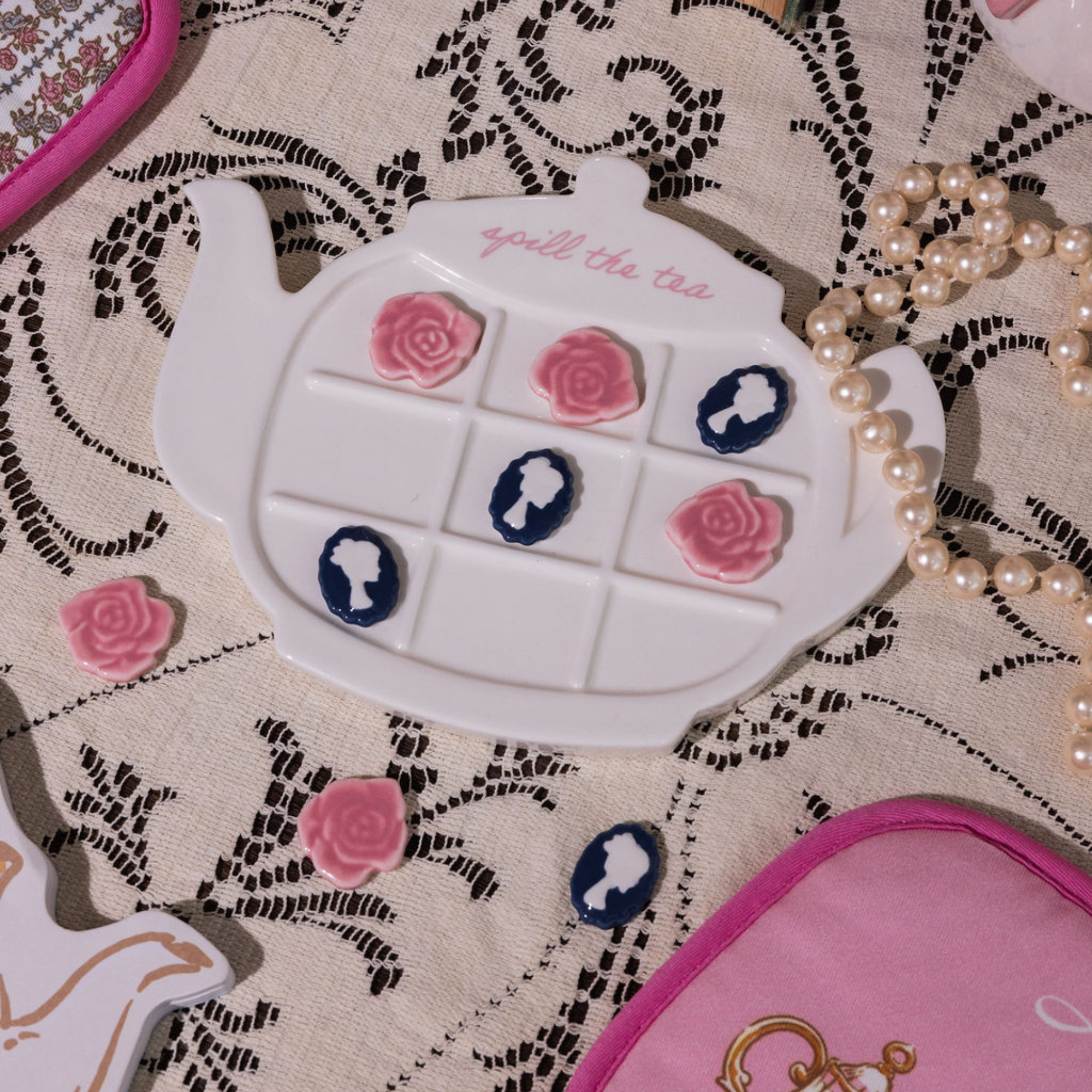 Teapot-shaped tic-tac-toe game with floral designs on a lace tablecloth